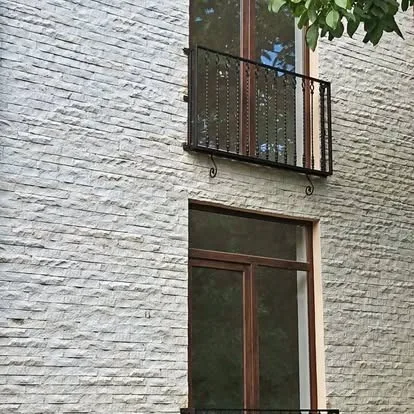 Exterior wall with light grey stacked stone veneer, wood windows, and iron balcony detail