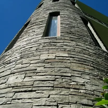 Curved stacked-stone tower with narrow vertical window under a clear blue sky