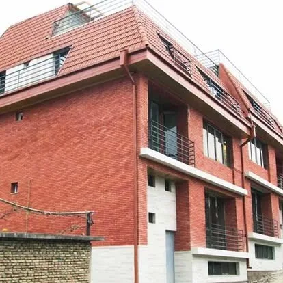 Modern multi-story building with red brick upper facade and light stone cladding at the base